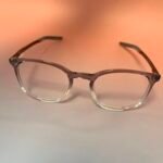 Clear-framed eyeglasses with brown temples resting on a peach gradient background.