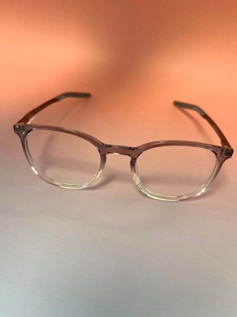 Clear-framed eyeglasses with brown temples resting on a peach gradient background.