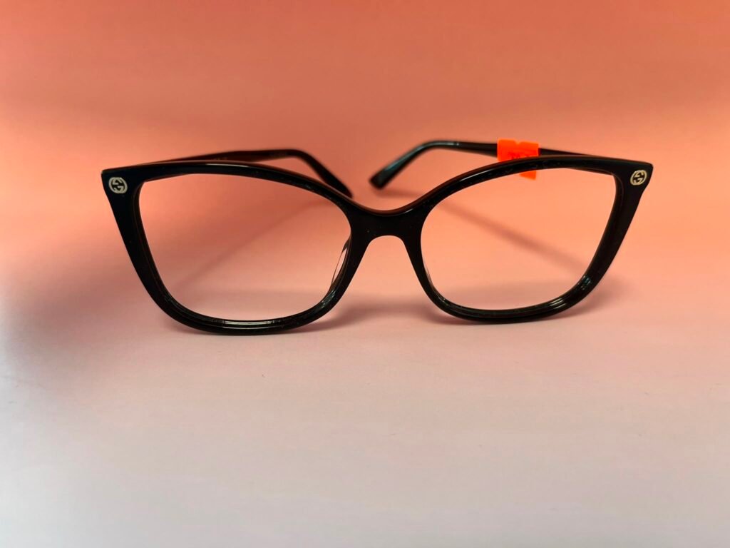 Black plastic eyeglasses with a small orange tag on the right temple, against a peach background.