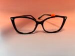 Black plastic eyeglasses with a small orange tag on the right temple, against a peach background.