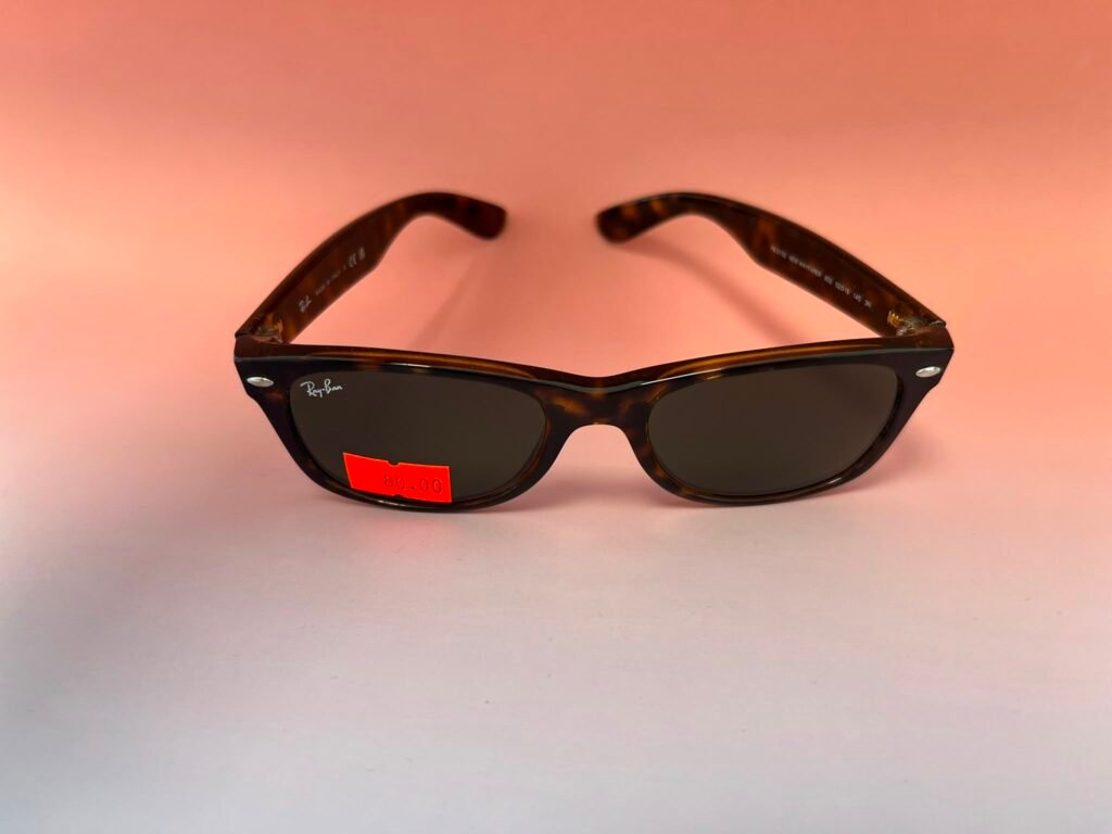 Ray-Ban tortoiseshell sunglasses on a pink background with a red price sticker showing 80.00 on the lens area