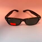 Ray-Ban tortoiseshell sunglasses on a pink background with a red price sticker showing 80.00 on the lens area