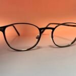 Close-up of black round eyeglasses resting on a warm orange background.
