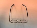 Eyeglasses with a metal frame and raised temples against a pink background (hanging posture).