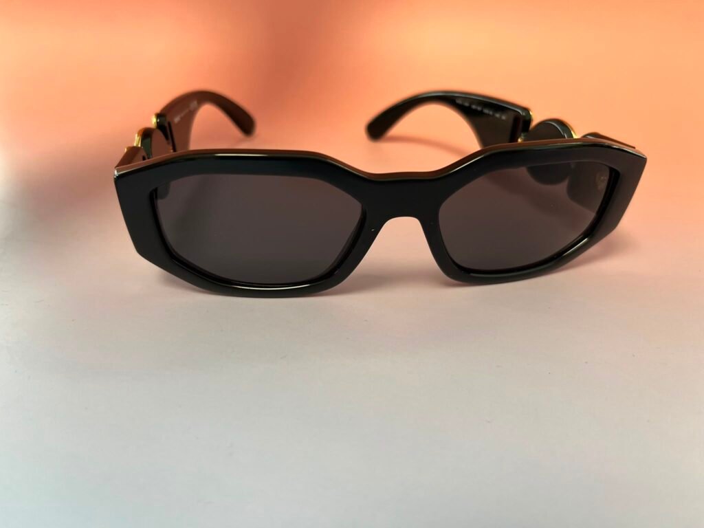 Close-up of black oversized sunglasses with gold accents on a peach to white gradient background