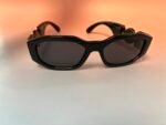 Close-up of black oversized sunglasses with gold accents on a peach to white gradient background