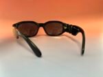 Close-up of black sunglasses lying on a gradient orange-to-white background, showing the curved frame and dark lenses.