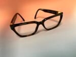 Tortoiseshell eyeglasses resting on a light surface with an orange gradient backdrop.