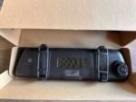Black dash camera packaged in an open brown cardboard box, lens visible on the right side of the device