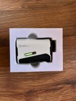Close-up of a white AimL12 device partially removed from its foam packaging on a wooden surface, with a green indicator light showing.