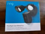 Ring Floodlight Cam Wired Plus packaging showing the two floodlight cameras on a blue box surface.Outdoor security camera product box labeled Ring Floodlight Cam Wired Plus with LED lights and siren.