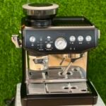 Espresso machine on a counter with a portafilter attached to the group head and a pressure gauge on the front panel.