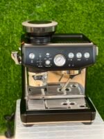 Espresso machine on a counter with a portafilter attached to the group head and a pressure gauge on the front panel.