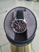 Citizen wristwatch with black leather strap resting in a gray display case cushion, stainless steel case and dark dial with multiple subdials.