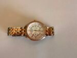 Gold and silver wristwatch with a diamond-studded bezel resting on a beige surface.