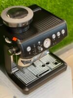 Close-up of a black espresso machine with a silver portafilter attached and a drip tray, ready to brew.
