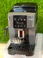 DeLonghi Magnifica Start espresso machine with glossy black control panel and bean-tray area visible, set against a green background