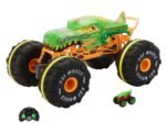 Green monster-truck toy with oversized black tires and orange chassis, shown with its remote and a small matching car beside it.