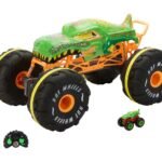 Green monster-truck toy with oversized black tires and orange chassis, shown with its remote and a small matching car beside it.