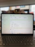 Laptop screen displaying Windows 11 System > About with hardware specs visible, keyboard in foreground