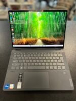 Open laptop on a dark table showing a vibrant bamboo forest wallpaper on the screen, keyboard in the foreground