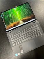 Laptop with a vivid bamboo forest wallpaper on the screen, resting on a dark textured surface.